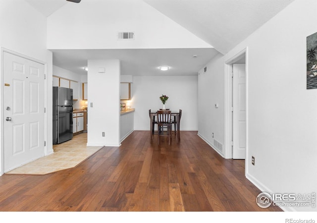 unfurnished living room with high vaulted ceiling, wood-type flooring, visible vents, and baseboards