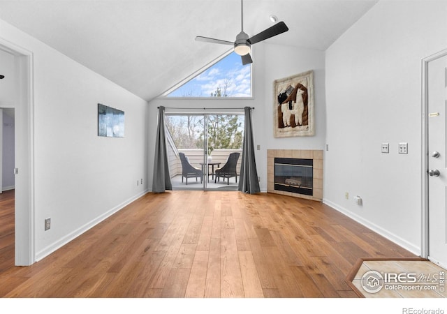 unfurnished living room with baseboards, a tiled fireplace, ceiling fan, vaulted ceiling, and light wood-style floors