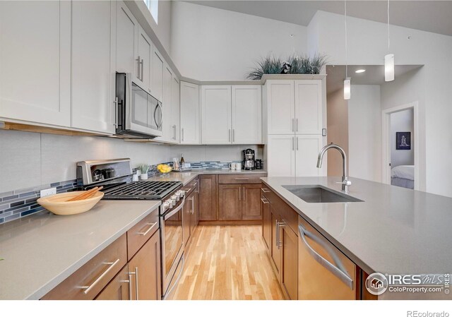 kitchen featuring light wood-style flooring, stainless steel appliances, a sink, hanging light fixtures, and decorative backsplash