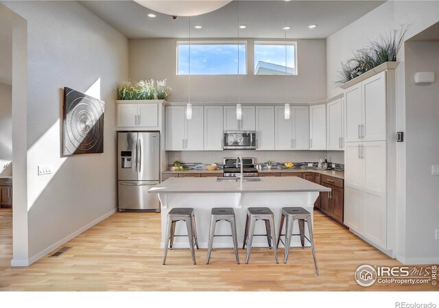 kitchen with a breakfast bar, a towering ceiling, appliances with stainless steel finishes, a sink, and light wood-type flooring