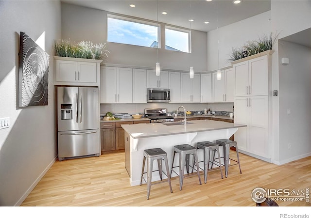 kitchen with a towering ceiling, appliances with stainless steel finishes, a kitchen island with sink, a sink, and a kitchen breakfast bar