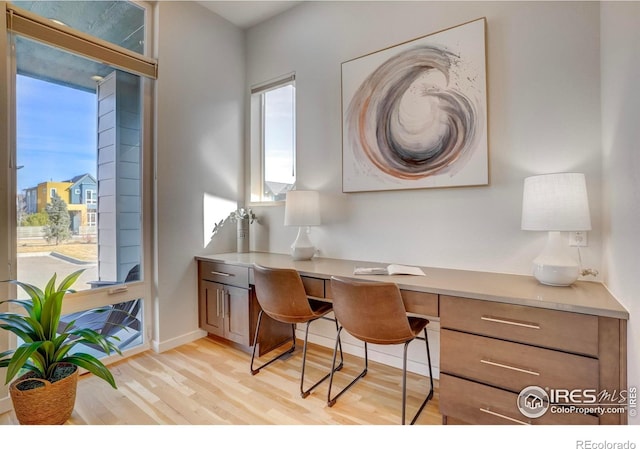 office area with light wood finished floors, baseboards, and built in desk