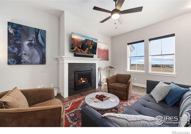 living room with a fireplace with flush hearth, a ceiling fan, baseboards, and wood finished floors