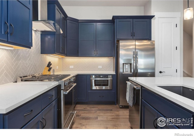2748 Prairie Flax St, Berthoud, CO 80513 - kitchen with wall chimney range hood, light countertops, dark wood-type flooring, appliances with stainless steel finishes, and blue cabinets