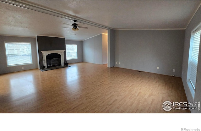 unfurnished living room with wood finished floors, visible vents, a ceiling fan, ornamental molding, and a glass covered fireplace