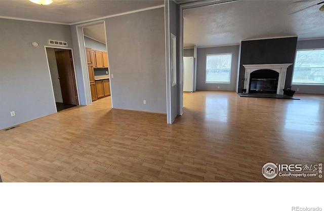 unfurnished living room featuring ornamental molding, a glass covered fireplace, visible vents, and plenty of natural light