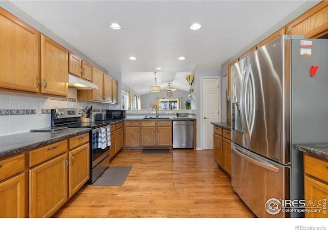 kitchen with lofted ceiling, under cabinet range hood, appliances with stainless steel finishes, light wood-type flooring, and backsplash