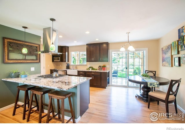 kitchen featuring a breakfast bar, island exhaust hood, light wood-style flooring, dark brown cabinets, and baseboards