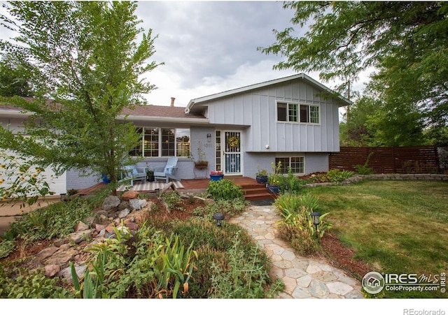 tri-level home featuring a deck, brick siding, fence, a front lawn, and board and batten siding