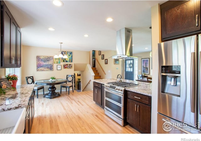 kitchen featuring dark brown cabinetry, appliances with stainless steel finishes, light stone counters, island exhaust hood, and light wood-style floors