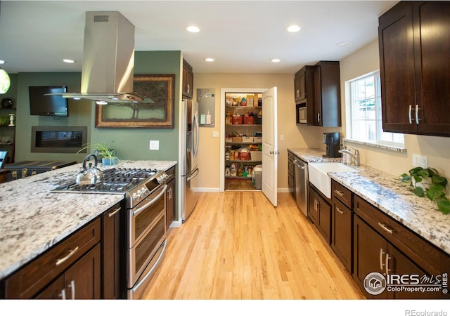 kitchen featuring island exhaust hood, appliances with stainless steel finishes, a sink, dark brown cabinets, and light wood-type flooring