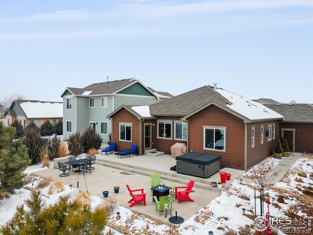 snow covered rear of property with entry steps, a hot tub, and a patio