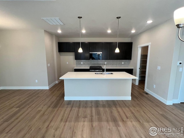 kitchen featuring a sink, light countertops, dark cabinetry, light wood-type flooring, and tasteful backsplash