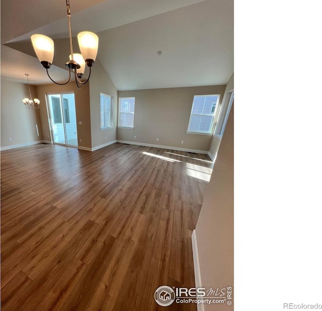 empty room with wood finished floors, vaulted ceiling, baseboards, and an inviting chandelier