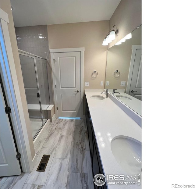 bathroom with double vanity, a shower stall, visible vents, and a sink