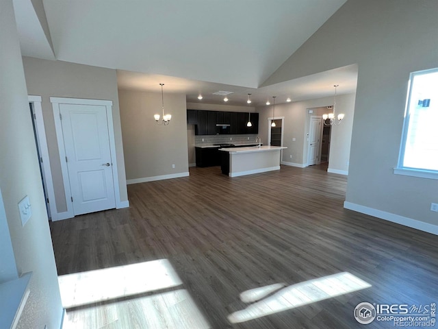 unfurnished living room featuring dark wood-style floors, a sink, a notable chandelier, and baseboards