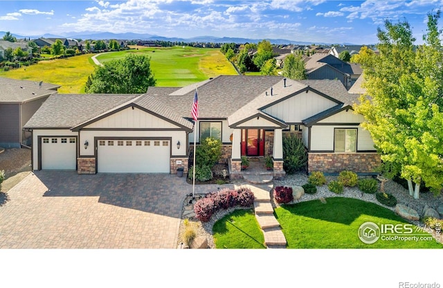 view of front of house featuring an attached garage, a mountain view, stone siding, roof with shingles, and decorative driveway