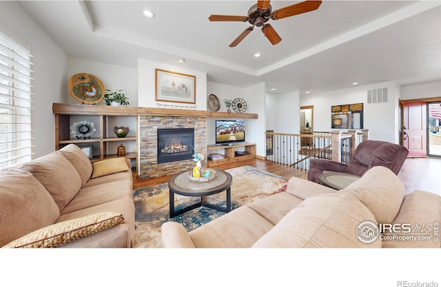 living room with a stone fireplace, recessed lighting, wood finished floors, visible vents, and a raised ceiling