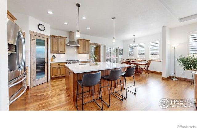 kitchen featuring light wood-style floors, backsplash, wall chimney range hood, and stainless steel fridge with ice dispenser