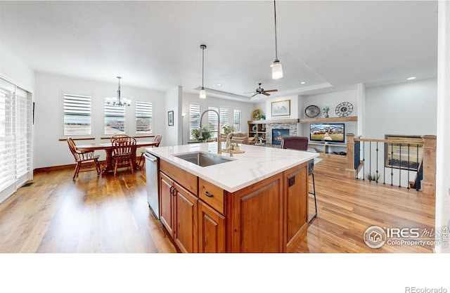 kitchen featuring light wood finished floors, dishwasher, a glass covered fireplace, brown cabinets, and a sink