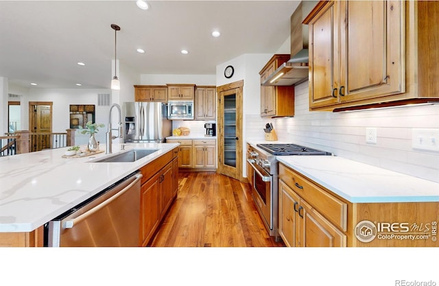 kitchen with light wood-style floors, appliances with stainless steel finishes, a sink, wall chimney range hood, and backsplash