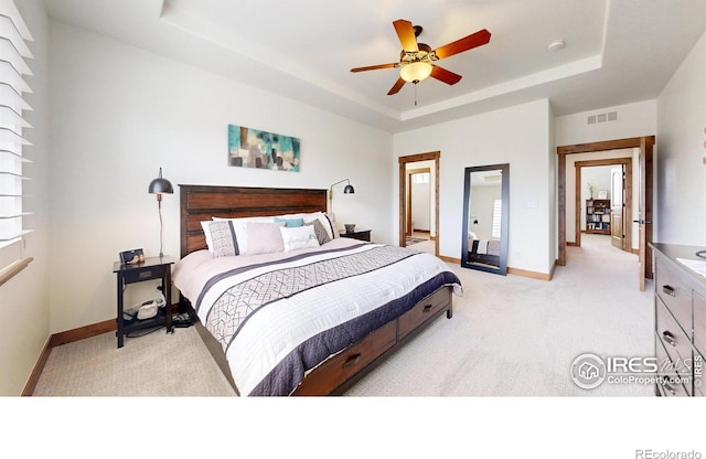 bedroom with baseboards, visible vents, a raised ceiling, and light colored carpet