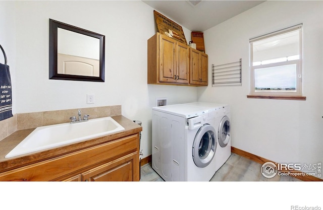 clothes washing area with a sink, washing machine and dryer, cabinet space, and baseboards