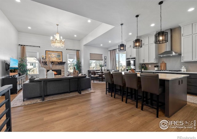 kitchen featuring a fireplace, light wood finished floors, light countertops, open floor plan, and wall chimney range hood