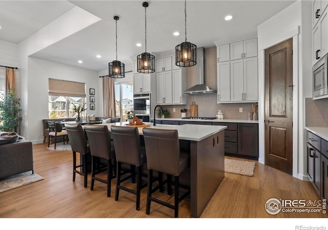 kitchen with open floor plan, wall chimney exhaust hood, tasteful backsplash, and light countertops