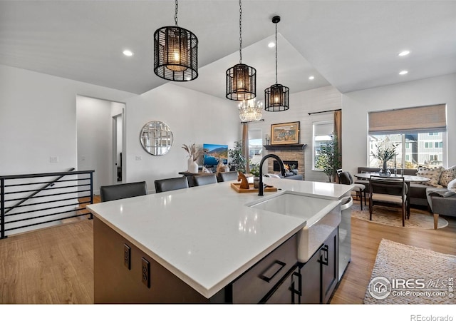 kitchen with open floor plan, a stone fireplace, light wood-style floors, pendant lighting, and a sink