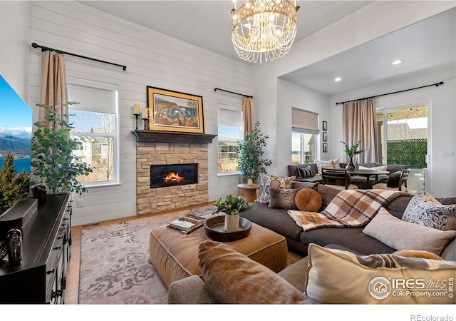 living room with recessed lighting, wood finished floors, a stone fireplace, and an inviting chandelier