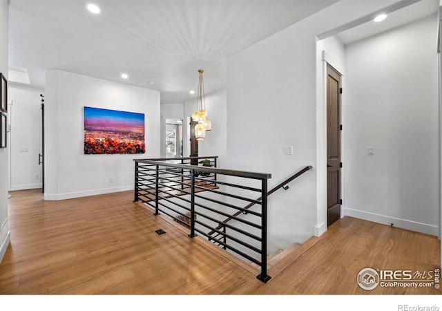 corridor featuring light wood finished floors, recessed lighting, baseboards, and an upstairs landing