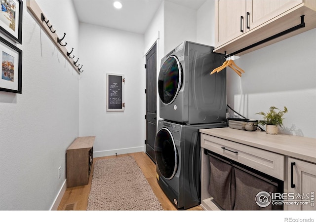 washroom featuring baseboards, cabinet space, light wood-style flooring, and stacked washer / drying machine