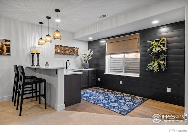 bar featuring visible vents, decorative light fixtures, wet bar, light wood-type flooring, and a sink