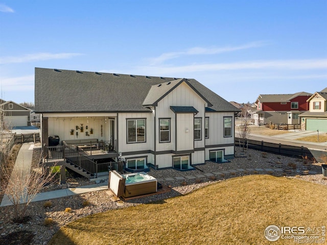 rear view of house with a deck, roof with shingles, stairs, and a hot tub