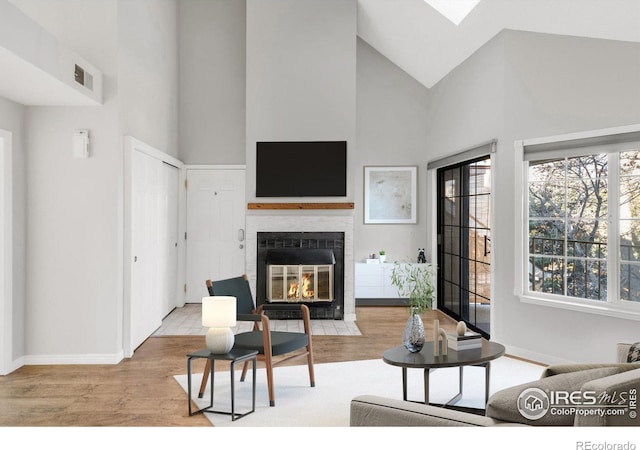 living area featuring a fireplace with flush hearth, high vaulted ceiling, baseboards, and wood finished floors