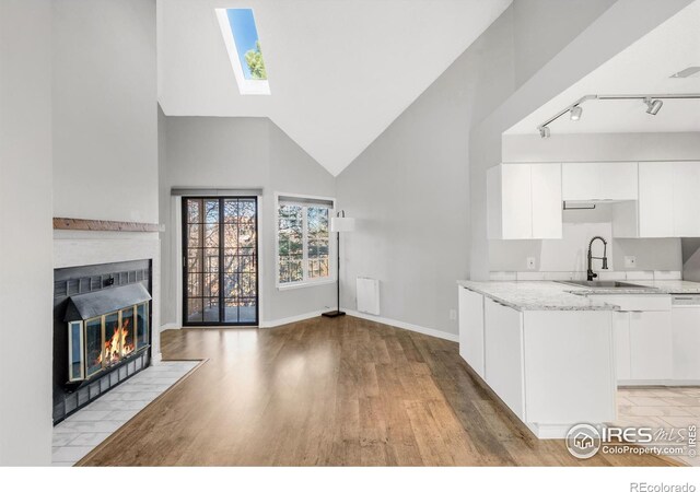 kitchen with light wood finished floors, white cabinets, light stone countertops, a fireplace, and a sink