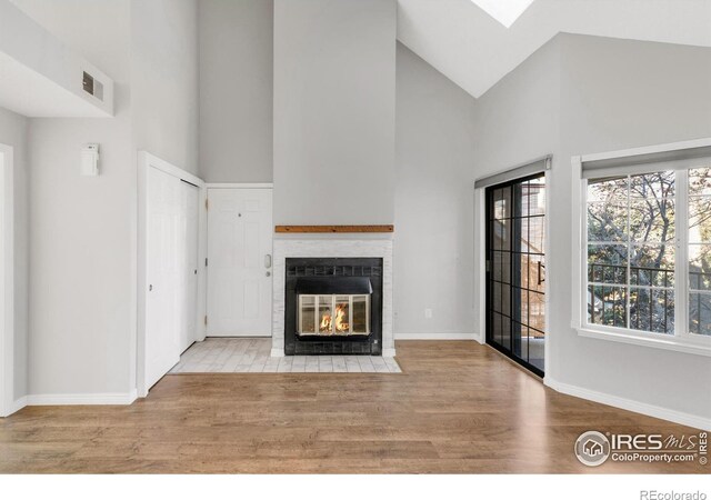 unfurnished living room featuring baseboards, a fireplace with flush hearth, high vaulted ceiling, and wood finished floors