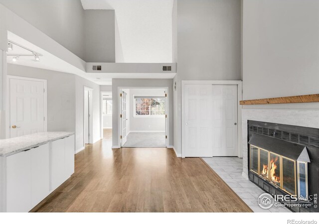 unfurnished living room with light wood-type flooring, visible vents, a fireplace, and a towering ceiling