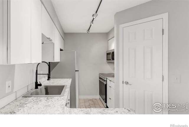 kitchen featuring stainless steel appliances, light countertops, white cabinets, a sink, and track lighting