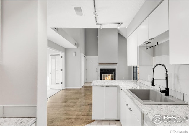 kitchen with white cabinets, a glass covered fireplace, a peninsula, light countertops, and a sink