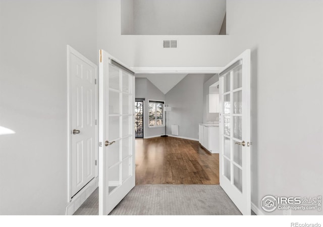 corridor with high vaulted ceiling, french doors, wood finished floors, and visible vents