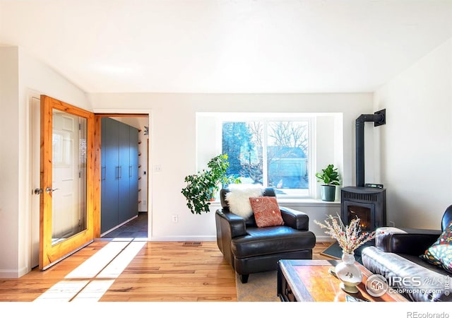 living area featuring light wood-style floors, a wood stove, and baseboards