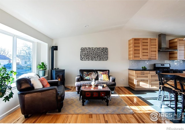 living room with light wood-style floors, a wood stove, vaulted ceiling, and baseboards