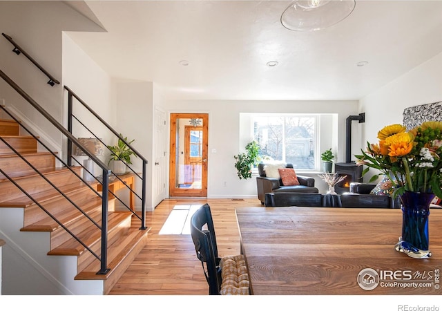 foyer with a wood stove, light wood-style flooring, baseboards, and stairs