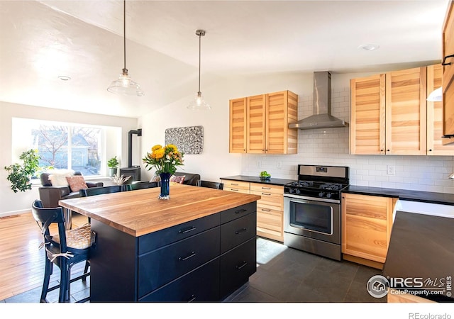 kitchen featuring tasteful backsplash, wall chimney exhaust hood, wood counters, a kitchen breakfast bar, and stainless steel range with gas cooktop