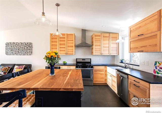 kitchen featuring stainless steel appliances, vaulted ceiling, light brown cabinetry, decorative backsplash, and wall chimney exhaust hood