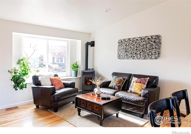 living room with a wood stove, visible vents, baseboards, and wood finished floors