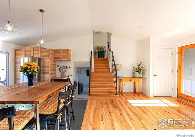 dining room with stairs, vaulted ceiling, and light wood-style floors