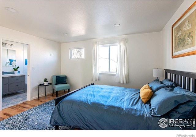 bedroom featuring baseboards, ensuite bath, and light wood finished floors